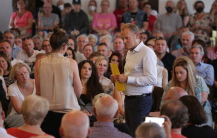Donald Tusk podczas spotkania z wyborcami stoi z mikrofonem wśród ludzi