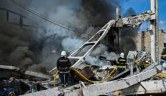 Palćy się zrujnowany ostrzałem budynek, strażak gasi ogień wodą z węża strażackiego