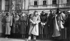 Piłsudski w wojskowym płaszczu i czapce, za nim wojskowiz