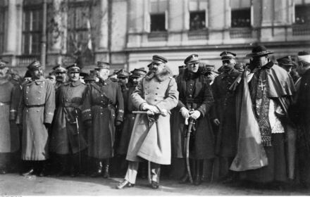 Piłsudski w wojskowym płaszczu i czapce, za nim wojskowiz