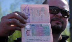 Mężczyzna w ciemnych okularach trzyma rosyjski paszport z anulowaną wizą