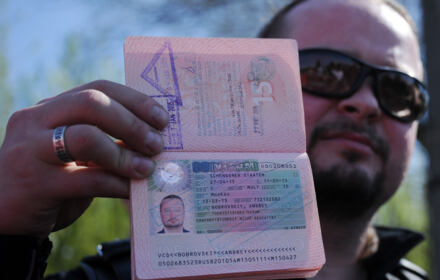 Mężczyzna w ciemnych okularach trzyma rosyjski paszport z anulowaną wizą