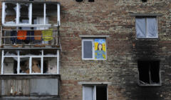 Zniszczony dom, w oknie - rysunek przedstawiający kobietę w niebieskim i żółtym kolorze (barwach Ukrainy)