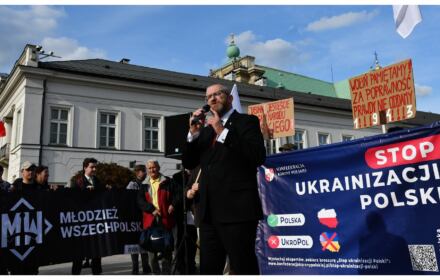 Poseł KOnfederacji Grzegorz Braun stoi z mikrofonem przed transparentem "Ukrainizacja Polski", obok inni ludzie