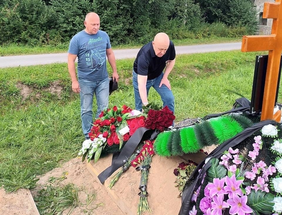 dwaj mężczyźni składają kwiaty na grobie