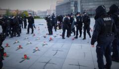 Policjanci wynoszą ludzi z placu, dpecząc po kwiatach, zniczach i narysowanych na płytach krzyżach